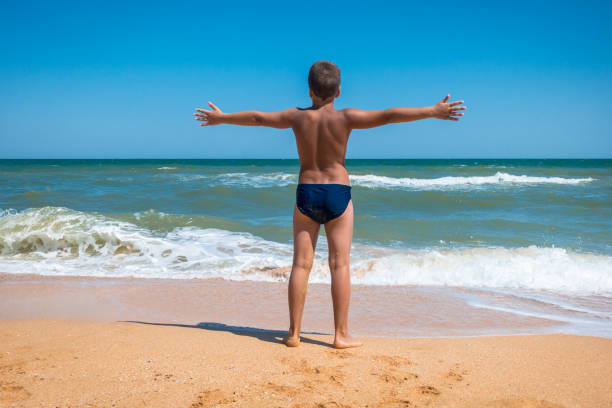 Adorable boy standing on the beach with his arms wide apart