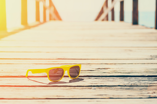 Vintage style - sunny yellow glasses on a wooden pier on a background of sun-drenched sea and ocean