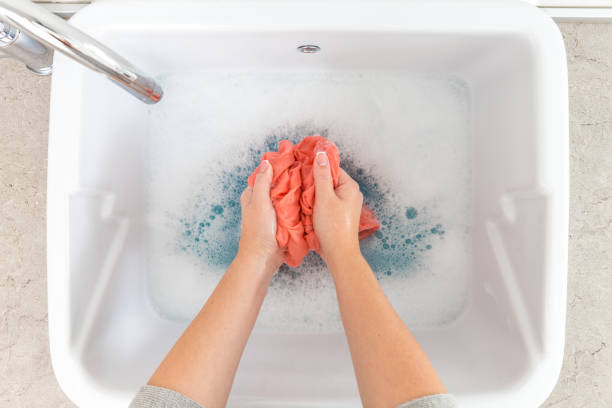 istock Female hands washing color clothes in sink 1026796542