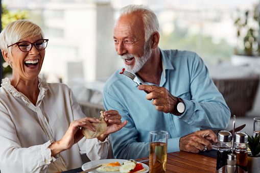 Senior Couple Having Breakfast On The Hotel Rooftop Restaurant. Senior man feeding woman and smiling.