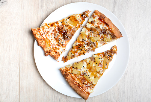 Three slices of chicken pizza with teriyaki sauce and pineapple lying on a white plate.
