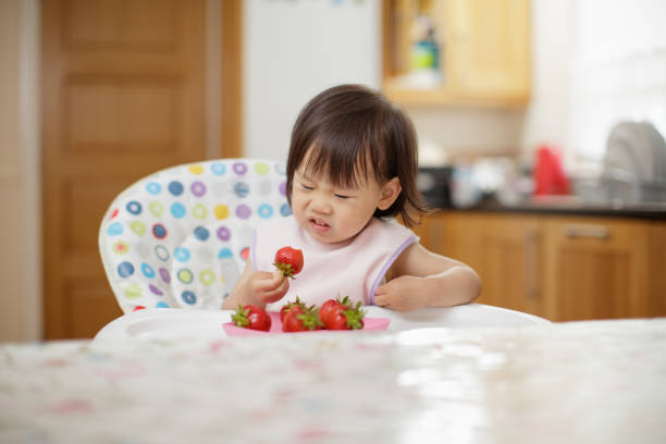 istock baby girl eating strewberry at home kitchen 1026828528