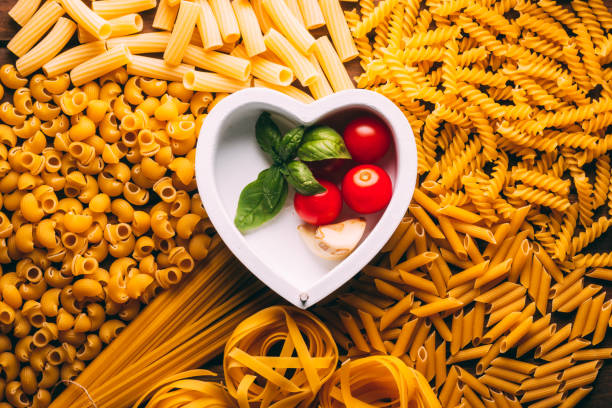 Table full of different types of pasta with a heart shape in the middle, pasta lovers stock photo