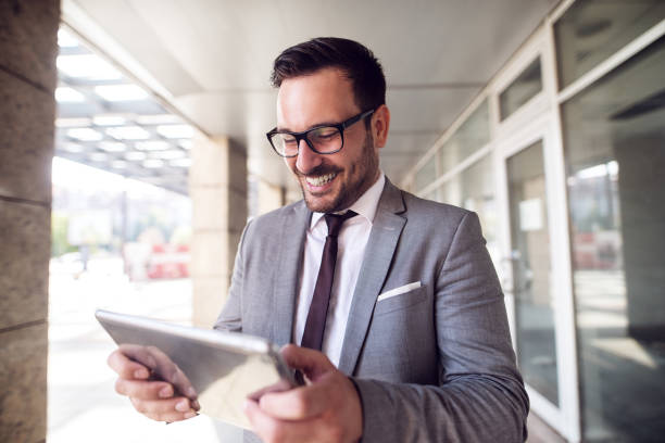istock Young modern businessman standing outside looking at his digital tablet with satisfaction on his face. Good day at work. 1026834614