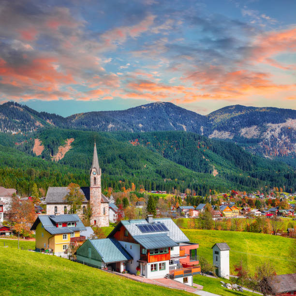 antastic charming Saint Primoz church, located atop a small hill in the picturesque Jamnik village of Slovenia, Europe. The church is beautifully lit by the golden hues of a stunning sunset, with the colorful mountain backdrop adding to the breathtaking scene. The photo was taken during the autumn season, and the trees surrounding the church are in full display of their warm and vibrant colorful fall colors.