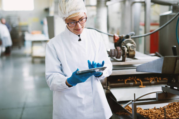 joven trabajadora con ropa estéril es comprobar la calidad de productos en fábrica de alimentos. - food and drink industry fotografías e imágenes de stock