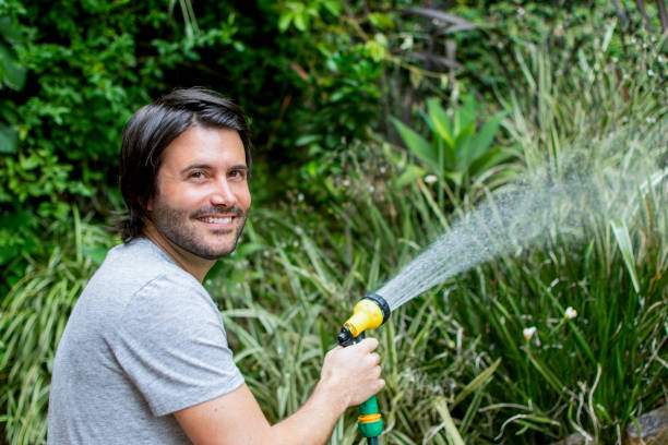 istock Man outdoors watering his garden with a hose 1026871706