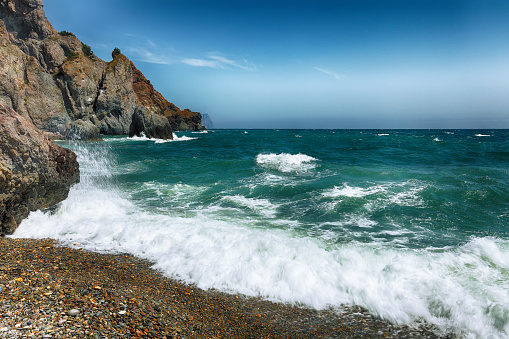 Sea waves crashing on the shore and flowing above seashore pebbles. Rocky seashore