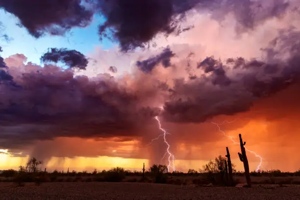 Lightning bolts strike from a colorful sunset storm in the Arizona desert landscape during the summer monsoon.