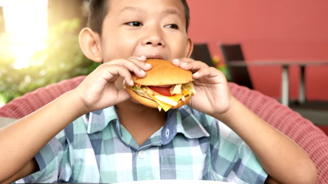 Cute asian boy are happy eating a hamburger in restaurant. Video 4k Slow motion