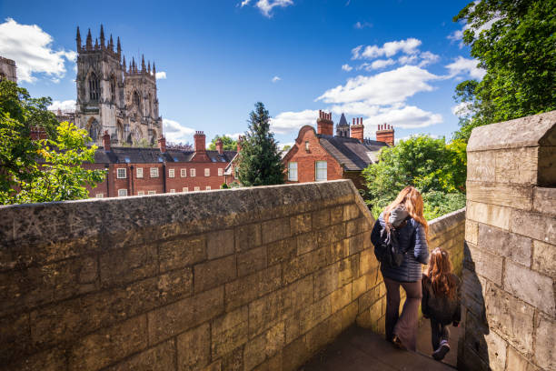 Tourists walking along York's city walls in England The mother and daughter are exploring the walls as they walk around the city. In the background, the grand York Minster can be seen. york yorkshire photos stock pictures, royalty-free photos & images