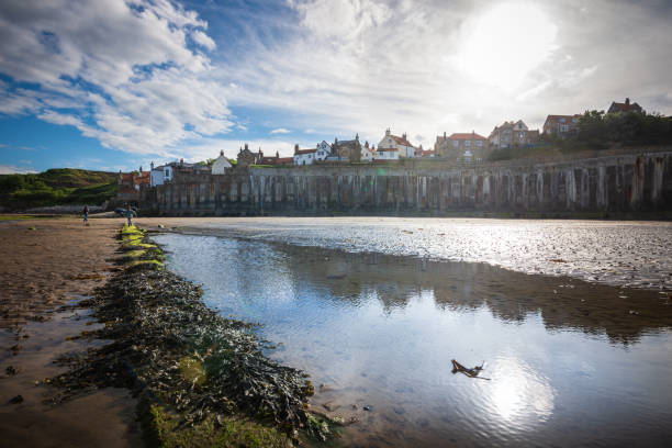 Robin Hood's Bay is an old fishing village on the Yorkshire coastline along England's East coast. Some tourists can be seen walking along the wet sands.