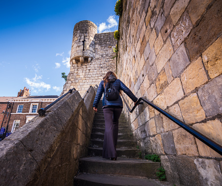 The woman is climbing up some stairs to explore the stone fortified walls, which surround the historic English city. She's traveling alone in the UK.