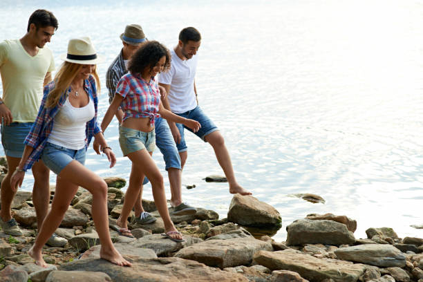 istock Joyful brave friends walking on stone shore and talking during countryside stroll, young people at lake 1026969758