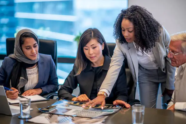 A group of businesspeople are having a meeting in an office. They are gathered around a table to look at documents.