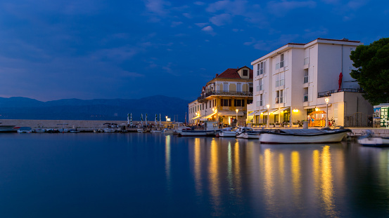 Croatian seaside town of Postira at night. Croatia, Dalmatia, Brac island.
Lights and restaurants and shops are illuminated in the town. Light is reflected in the sea. Summer travel destination. Long exposure. HDR photo