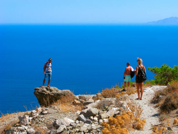Greece, Santorini. Young man stands on the cliff over the Aegean sea. This cliff is located on the top of the Mesa Vouno mountains. On top of Mesa Vouno located ruins of Ancient Thira (ancient capital of Santorini). Blue sea infiniti to the horizon. On the right is silhouette of Anafi Island.