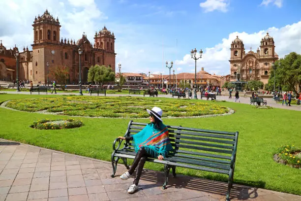 Female relaxing on a bench at Plaza de Armas with Cusco Cathedral and the Iglesia de la Compania de Jesus in background, Cusco, Peru