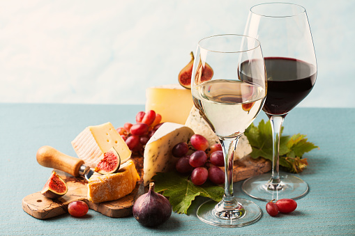Glasses of white and red wine and variety of cheeses on serving board