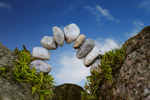 balanced stone arch of pebbles as zen symbol for a bridge or a gate, blue sky, selected focus