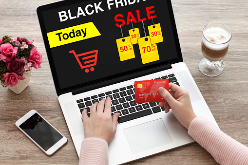 woman holding credit card typing laptop keyboard with sale black friday on screen