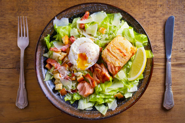 istock Salmon caesar salad. Crispy pan fried salmon fillet, bacon, poached egg, romaine lettuce and croutons in bowl on wooden table 1027078506