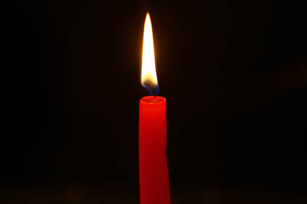 istock tiny wax lighting red candle with bright flame on the heavy black background. 1027097546