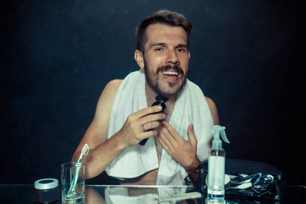 istock young man in bedroom sitting in front of the mirror scratching his beard 1027100202