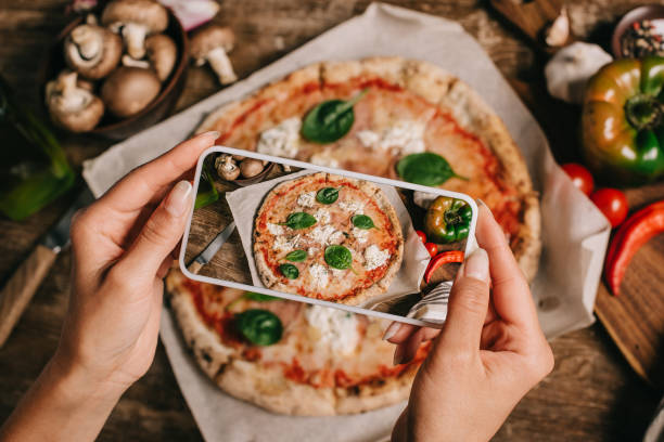 recortar el tiro de blogger de comida tomar foto de la pizza cocida en papel sobre la superficie de madera de horno - alimento fotos fotografías e imágenes de stock