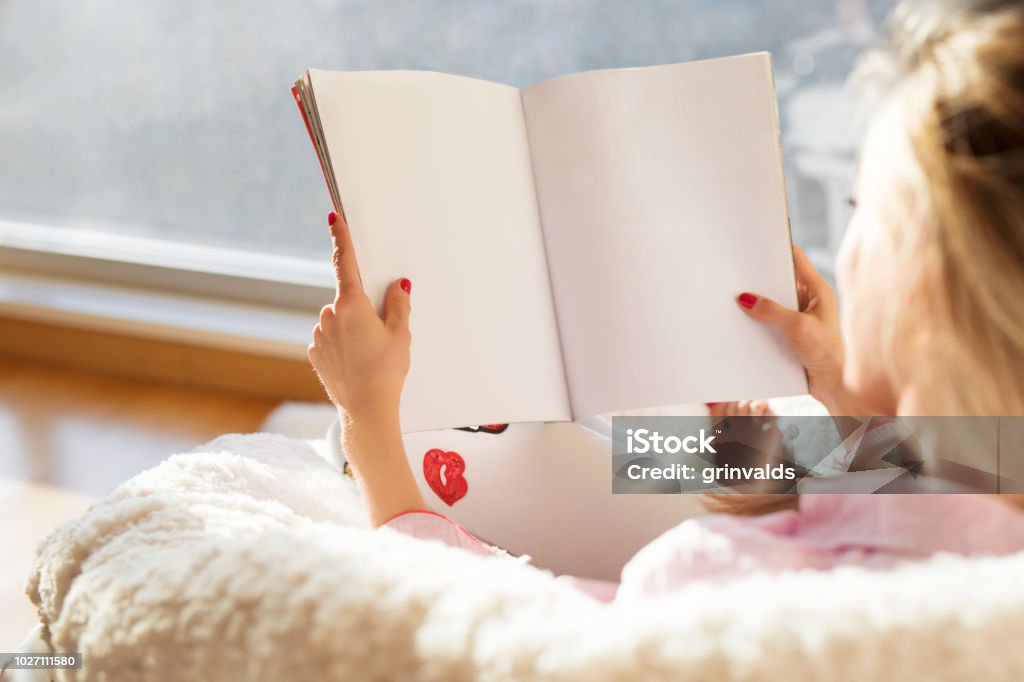 Woman reading magazine with empty white blank pages. Mockup and template for your own content. Woman reading magazine with empty white blank pages. Mockup and template for your own content. Photo from behind. Magazine - Publication Stock Photo