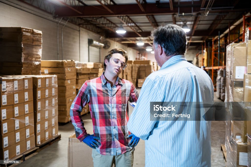 Ein Lagerleiter spricht mit einem jüngeren Lagerarbeiter. - Lizenzfrei Employee Stock-Foto