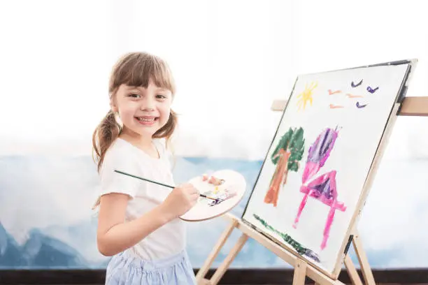 Cute little girl is painting on paper at home. Setup studio shooting.