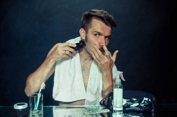 istock young man in bedroom sitting in front of the mirror scratching his beard 1027136120
