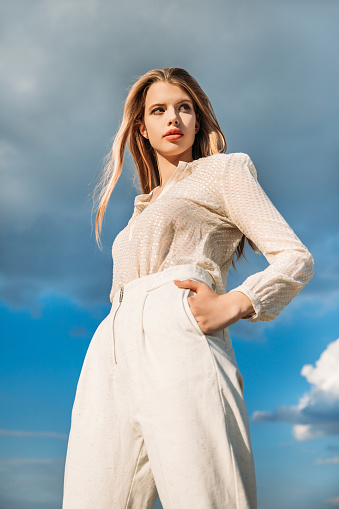 bottom view of elegant fashionable model posing in white stylish clothes with cloudy sky on background