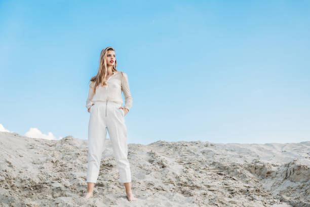 istock young elegant woman in white clothes posing on sand dune with blue sky 1027136536
