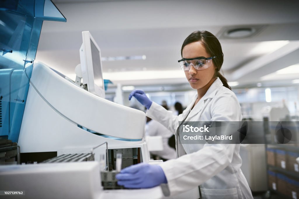 There’s always something waiting to be discovered Shot of a young woman using a machine to conduct a medical test in a laboratory Laboratory Stock Photo
