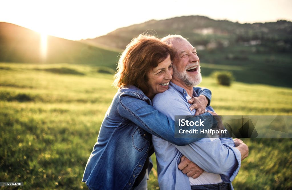 Vista lateral de pareja senior abrazar fuera en la naturaleza de la primavera al atardecer. - Foto de stock de Felicidad libre de derechos