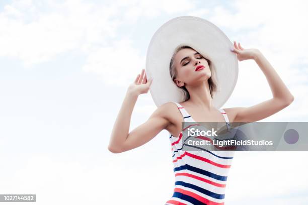 Modische Mädchen Posiert In Gestreiften Badeanzug Und Sommerhut Mit Sky Auf Hintergrund Stockfoto und mehr Bilder von Badebekleidung