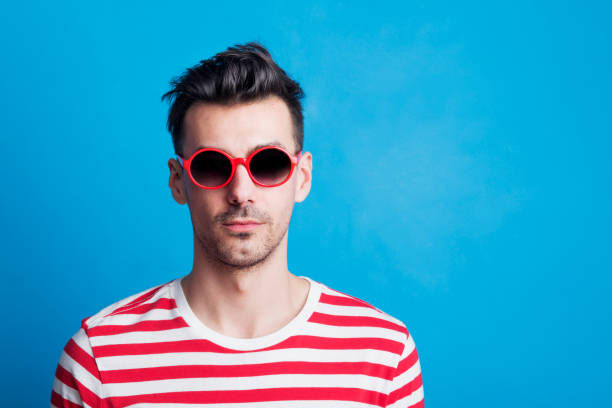 ritratto di giovane in uno studio con occhiali da sole su sfondo blu. - t shirt men red portrait foto e immagini stock