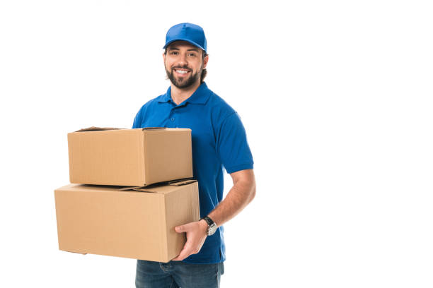 istock handsome happy young delivery man holding cardboard boxes and smiling at camera isolated on white 1027154078