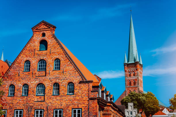 istock Red brick historical salt storehouse building. Church tower with ererald colored spire in background against blue sky. Luebeck, Schleswig-Holstein, northern Germany 1027157922