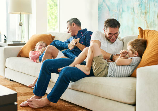 Getting their daily dose of tickles Full length shot of an affectionate family of four on the sofa at home gay man photos stock pictures, royalty-free photos & images