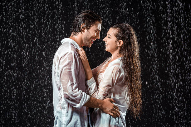 istock side view of smiling couple hugging while standing under rain isolated on black 1027166090