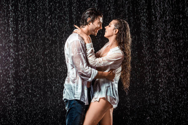istock side view of smiling couple hugging while standing under rain isolated on black 1027166118