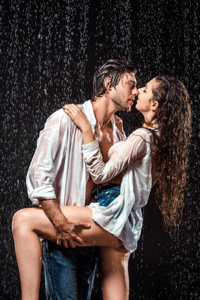 istock seductive wet couple in white shirts standing under rain isolated on black 1027168204