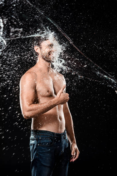 istock smiling young man showing thumb up while swilled with water isolated on black 1027169064