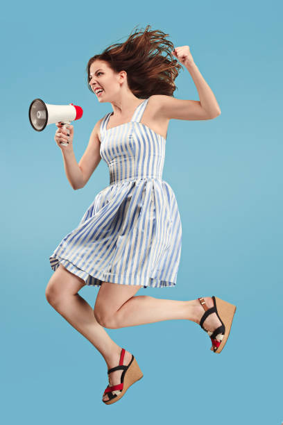 istock Beautiful young woman jumping with megaphone isolated over blue background 1027169158