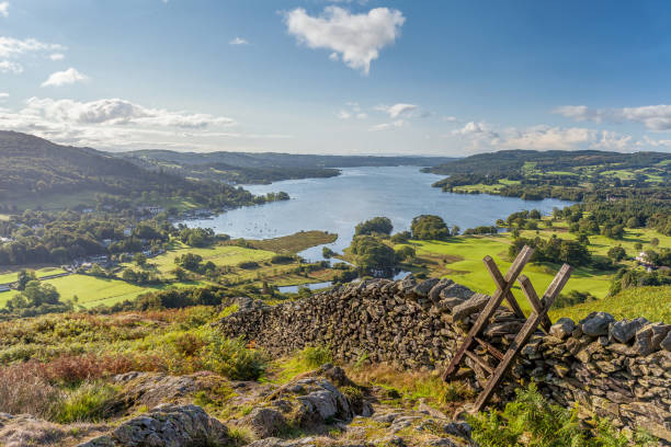 Lakeland View of Windermere from Loughrigg Fell. View of Windermere in the English Lake District taken from Loughrigg Fell. On a summer morning. With white fluffy clouds, shafts of Light on to Green fields with a Dry Stone Wall and wooden Style in the Foreground. cumbria photos stock pictures, royalty-free photos & images