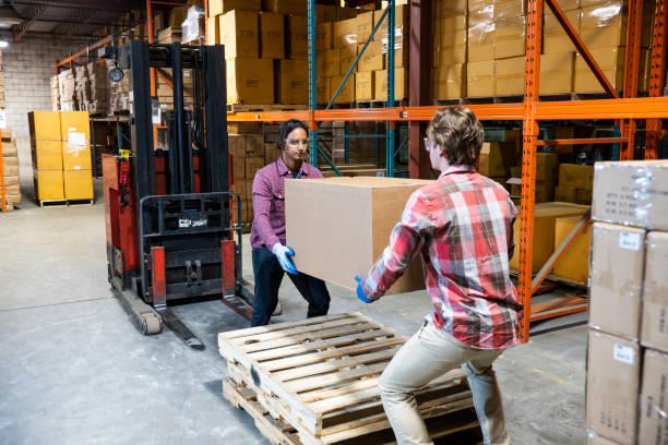 Two warehouse workers preparing to lift a heavy box together stock photo