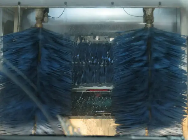 Photo of Car washing station with automatic rotating wash brushes in action. Automatic conveyorized tunnel car wash